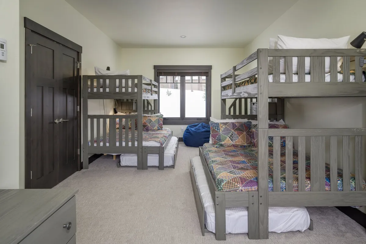 A lively bunk room with twin-over-full bunk beds, colorful quilts, a bean bag chair, and a wardrobe. The space feels playful and inviting, designed for kids’ enjoyment and group sleepovers.