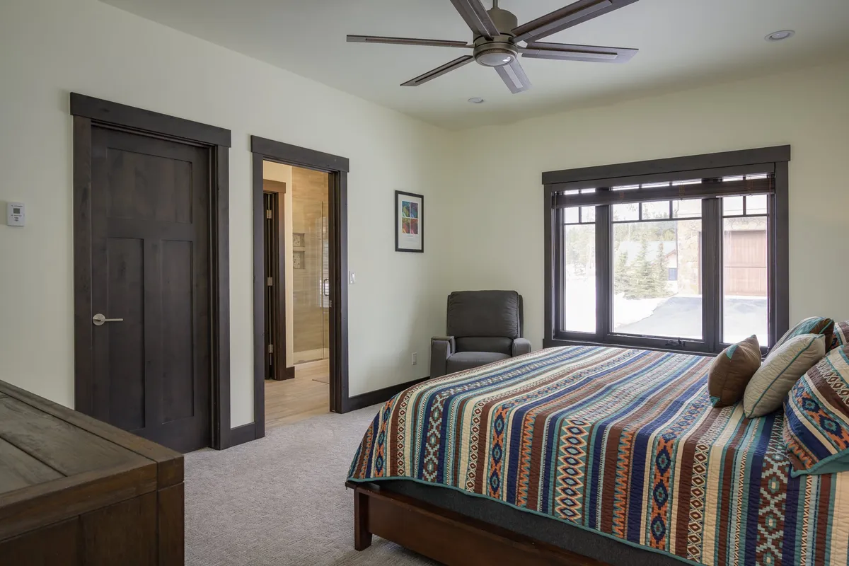 A cozy queen mini-suite featuring a bed with a colorful bedspread, a large window streaming in sunlight, and a comfortable reading chair. The atmosphere is warm and inviting.