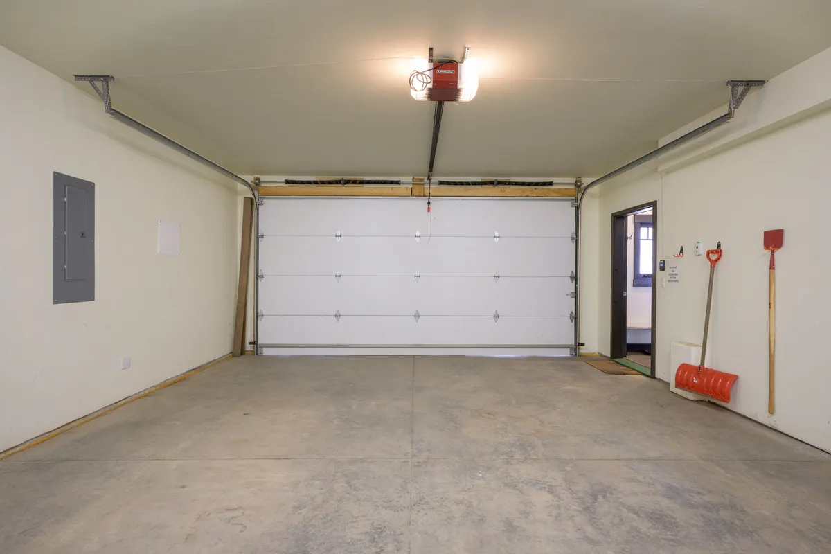 A view inside the garage, highlighting organized tool storage, a garage door, and a bright light fixture. The setup is ideal for storing and prepping outdoor gear before heading out for the day's adventures.