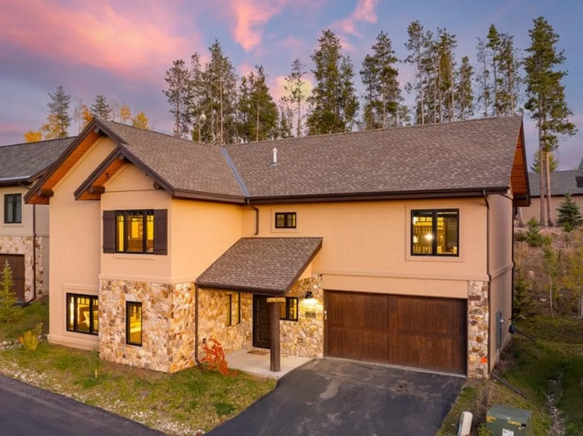 This image displays the welcoming stone facade of the cabin, accented by large windows and a spacious front porch. The outdoor space hints at both relaxation and gatherings, set against a tranquil neighborhood backdrop ideal for easy access to local trails and group activities.