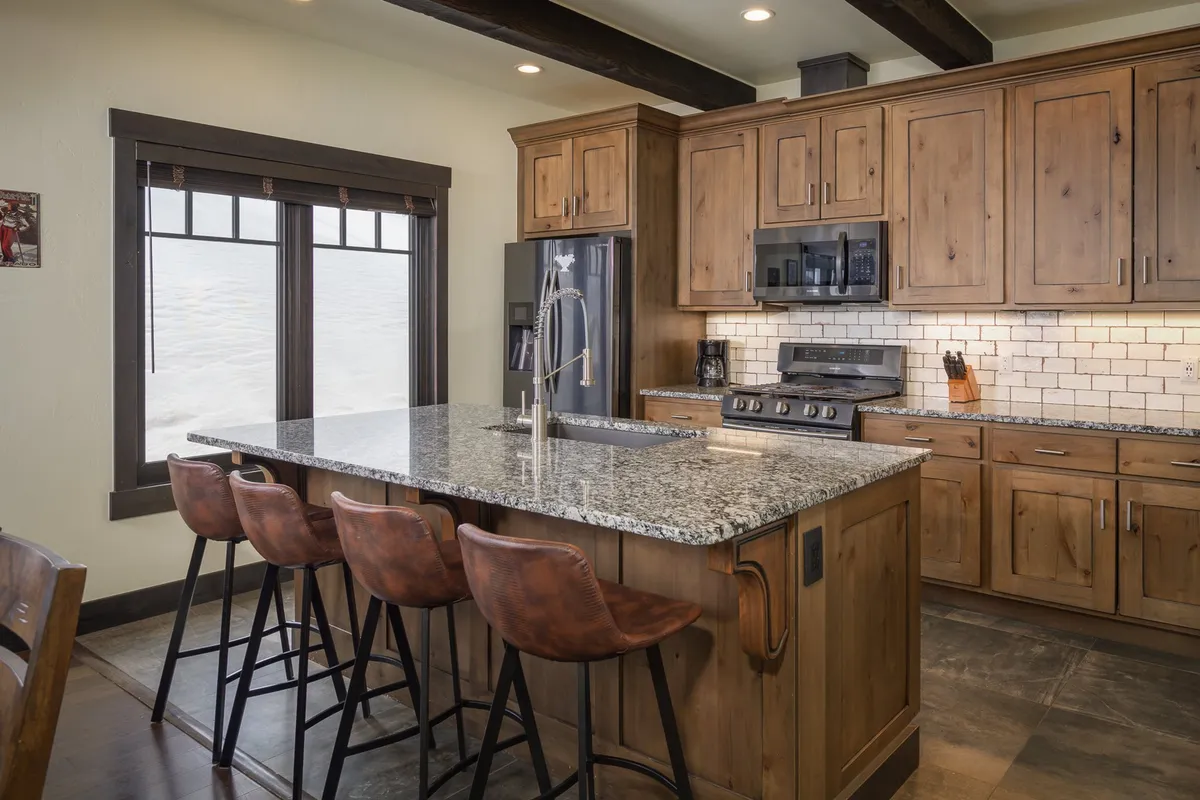 A beautifully appointed kitchen featuring a large granite island with bar stools, warm wooden cabinetry, and modern, premium stainless steel appliances. The open layout invites cooking, entertaining, and social gatherings.