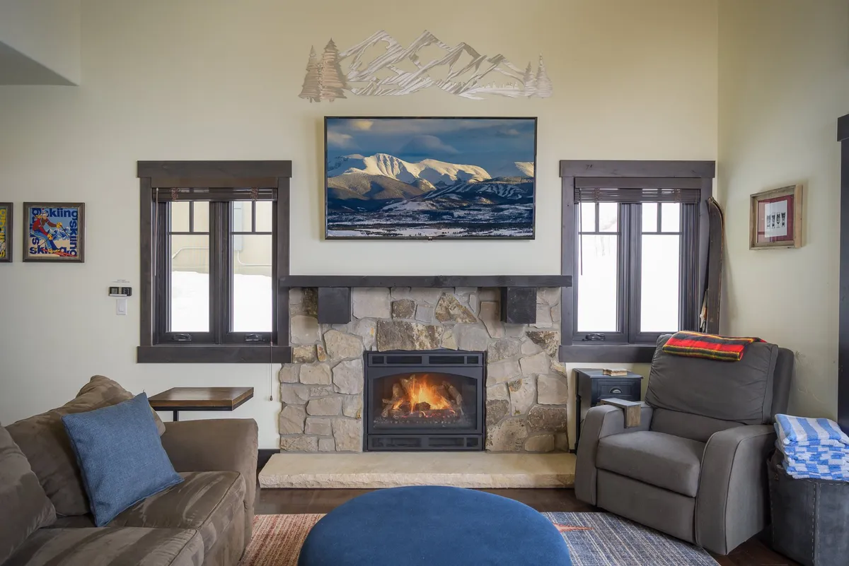 A cozy seating area arranged around a fireplace, complemented by mountain-themed artwork. Plush armchairs and a sofa offer ample space for relaxing, reading, or unwinding with loved ones, all enveloped in warm lighting.