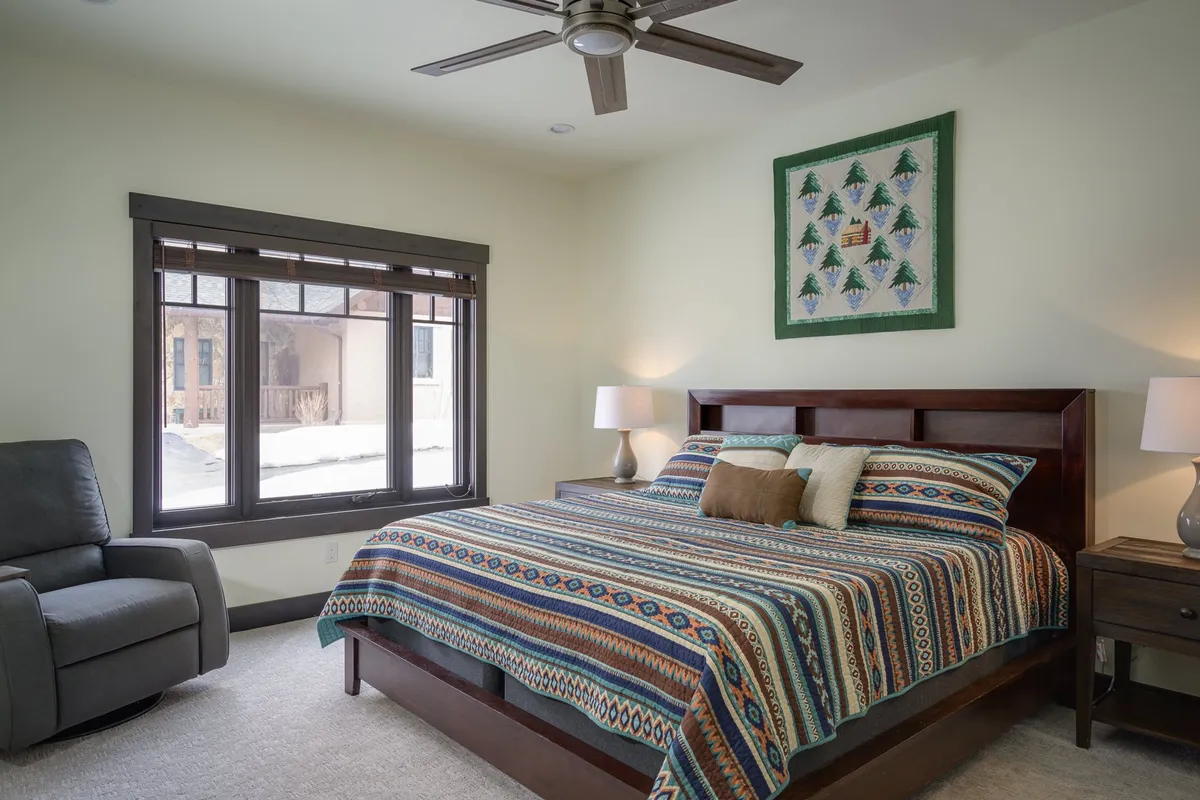 A serene bedroom featuring a bed with patterned bedding, a window letting in natural light, and a decorative quilt on the wall. The space exudes calm and comfort, ideal for restful nights.