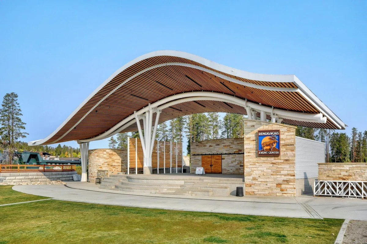 This exterior image showcases a contemporary curved roof structure, sturdy stone walls, and an open stage area, suggesting a lively setting for concerts, festivals, and community gatherings. The scene is bathed in natural light and invites viewers to imagine themselves participating in outdoor events and activities.