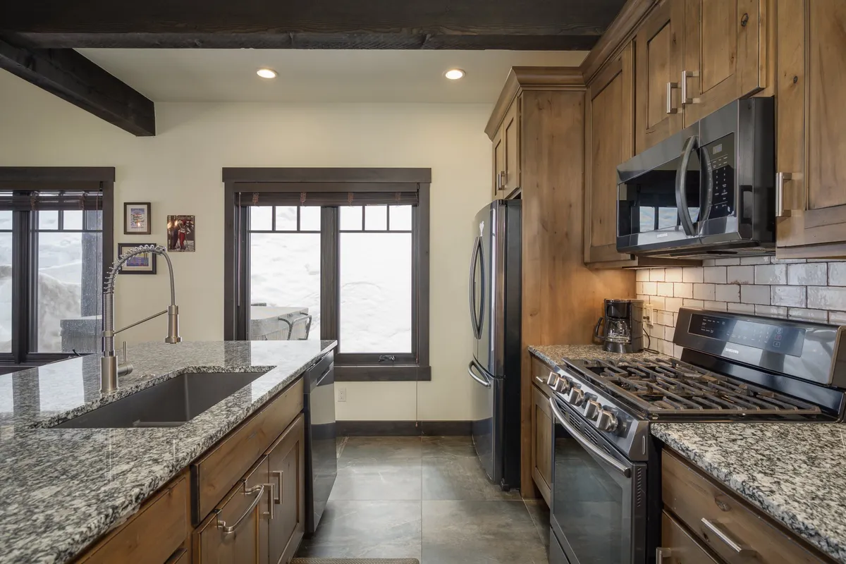 A cozy kitchen scene highlighting sleek granite countertops, stainless steel appliances, and wood cabinetry, with a snowy landscape visible outside the window. The ambiance suggests gatherings for meal prep and shared culinary moments.
